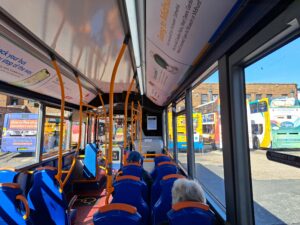 Interior of a bus with blue seats and orange grab rails, looking toward the front; outside are colorful buses in a depot.